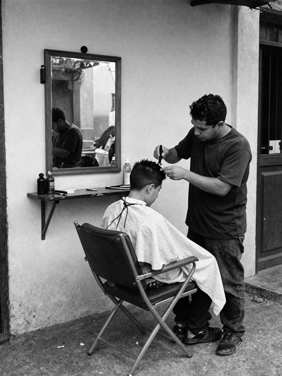 Barbero cortando el cabello a un niño afuera de su barbería